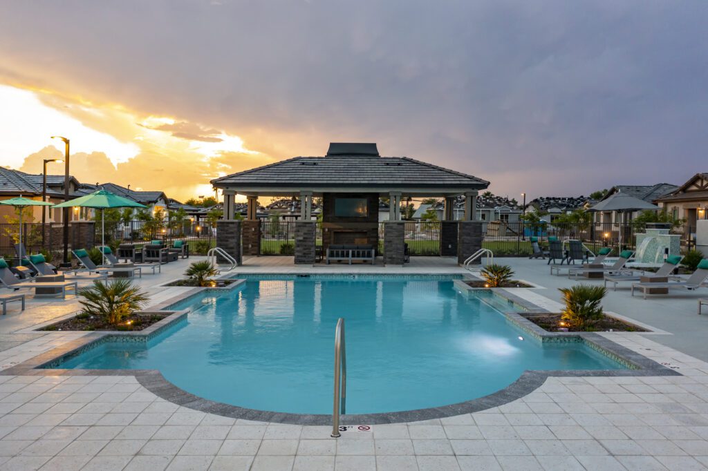Swimming pool at a residential home community with a central pavilion and seating area during sunset.